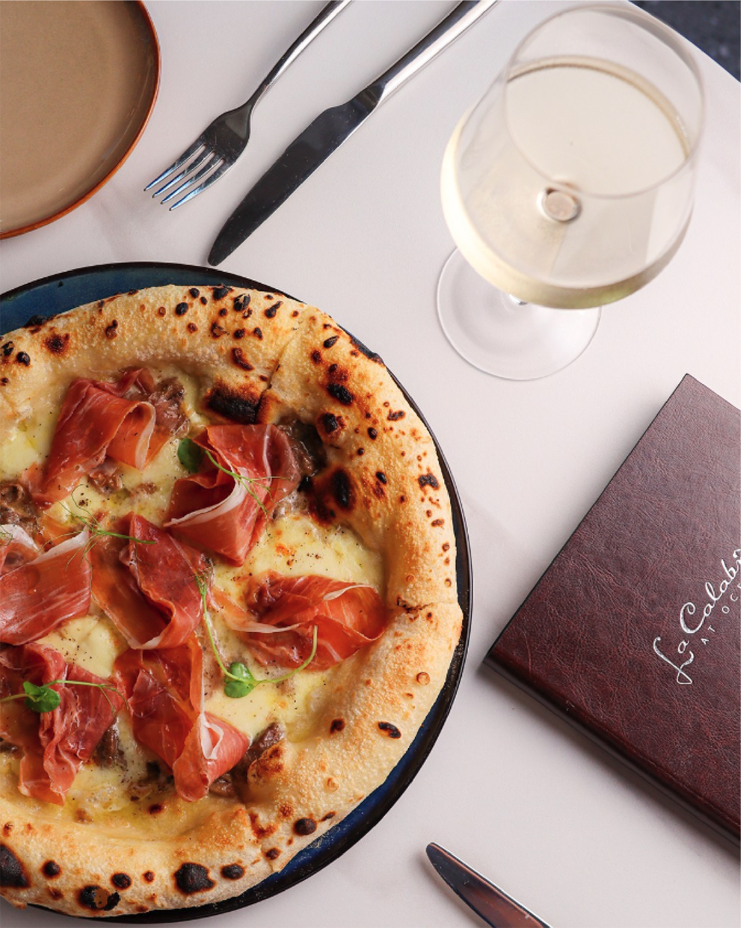 Post Instagram: pizza con prosciutto crudo servita con un calice di vino bianco